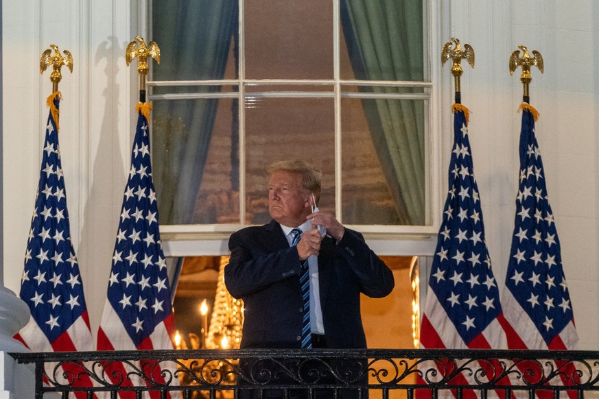 epa08723078 US President Donald J. Trump takes his face mask off after returning to the White House, in Washington, DC, USA, 05 October 2020, following several days at Walter Reed National Military Me ...