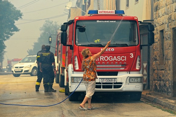 epa06094741 A woman sprays water in front of a fire truck while smoke caused by wildfires around Split blurs the scene in Split, Croatia, 18 July 2017. Croatian firemen try put the wildfires under con ...