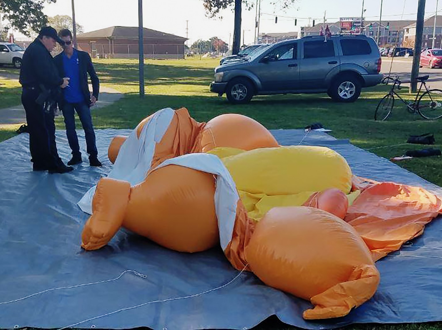 A responding officer and an unidentified man stands by a Baby Trump balloon deflated by someone at Monnish Park as people were protesting President Donald Trump&#039;s visit to an NCAA college footbal ...