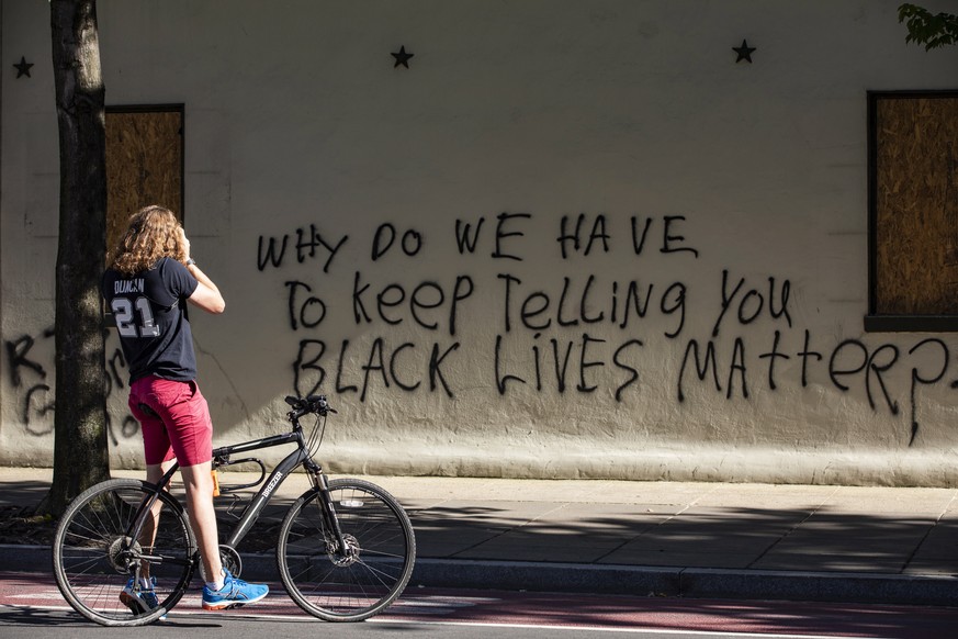 epa08459124 A cyclist stops to take a photo of protest graffiti on the side of a building during a demonstrations over the death of George Floyd, who died in police custody, near the White House in Wa ...