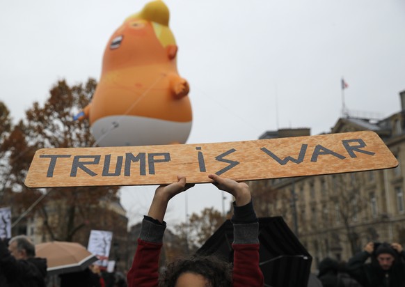 A child holds up a placard in front of a inflatable blimp depicting President Donald Trump in Republique square in Paris, Sunday Nov. 11, 2018 ahead of an anti-Trump gathering. President Trump joined  ...