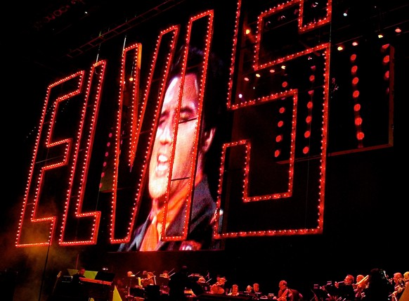 This Aug. 16, 2002 file photo shows an image of Elvis Presley singing as his band plays below at the start of the Elvis Presley 25th Anniversary Concert in Memphis, Tenn. The red Elvis sign is from th ...