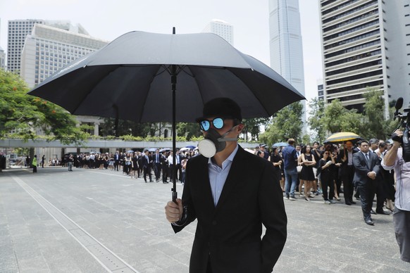 A man carries an umbrella and wears a face mask as lawyers gather for a protest march in Hong Kong, Wednesday, Aug. 7, 2019. The head of Beijing&#039;s Cabinet office responsible for Hong Kong says th ...
