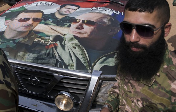 Syrian solder Hassan Muhammad stands near a car covered by a collage showing photos of faces of Russian President Vladimir Putin, right, Syrian President Bashar Assad, left, and a Syrian general, Pres ...