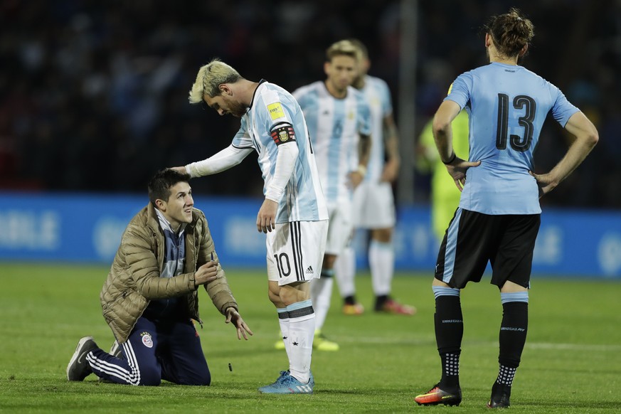 A fan who invaded the pitch kneels in front of Argentina&#039;s Lionel Messi, center, as Uruguay&#039;s Gaston Silva looks on during a 2018 Russia World Cup qualifying soccer match in Mendoza, Argenti ...