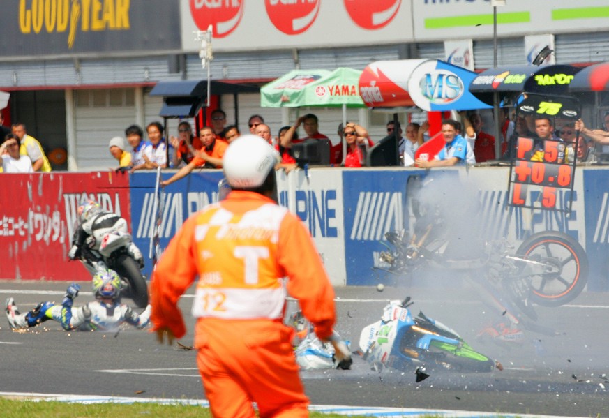 Spanish 125cc rider Sergio Gadea, left, slides on the race course after crashing with Swiss Thomas Luethi, partly seen behind a course marshal at center, during the the Grand Prix of Japan motorcyclin ...