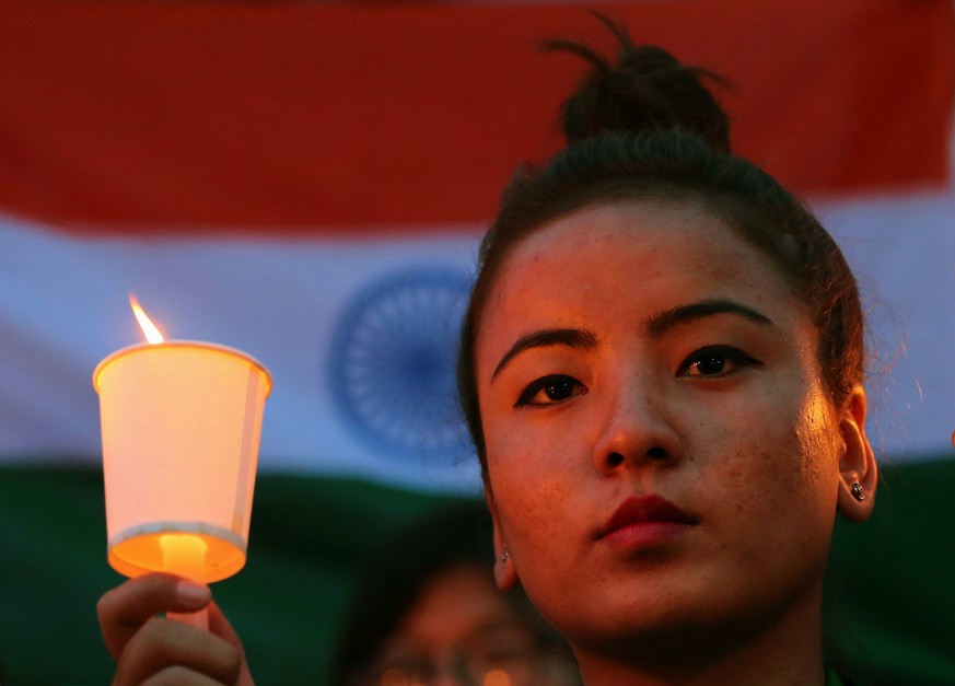 epa06677631 A Member of the Northeast People Voice India Foundation, a non-governmental organization, holds a candle in front of Indian tri colour flag during a candle light vigil as they condemned an ...