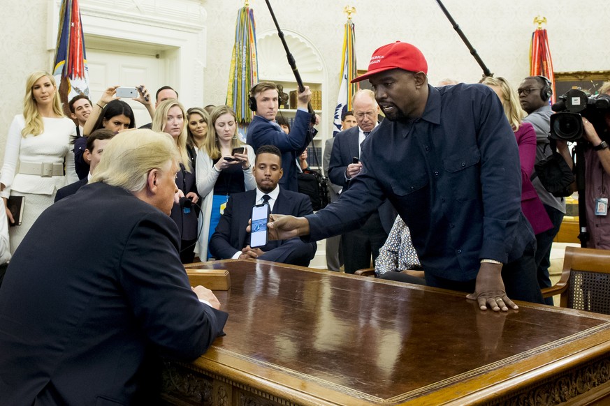 epa07086414 US entertainer Kanye West (R) shows a cell phone depicting the image of an aircraft to US President Donald J. Trump (L) during their meeting in the Oval Office of the White House in Washin ...