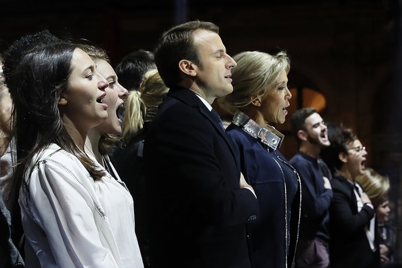 Incoming French President Emmanuel Macron, center left, and his wife Brigitte Macron, center right, sing the national anthem with supporters in front of the Pyramid at the Louvre Museum in front of th ...