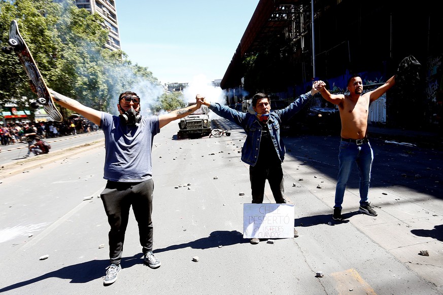 epa07939404 Demonstrators try to protect and avoid clashing with police members in a new day of mass protests at Plaza Italia, in Santiago, Chile, 21 October 2019. An unrest, sparked by a hike in metr ...