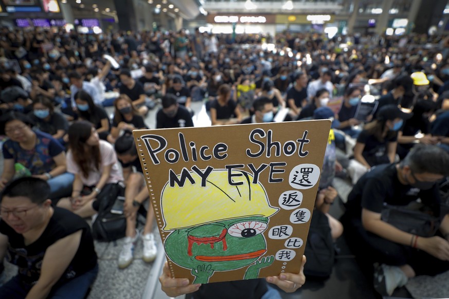 A protester displays a placard during a sit-in protest at the arrival hall of the Hong Kong International Airport in Hong Kong, Monday, Aug. 12, 2019. It is reported that police shot a woman in the ey ...