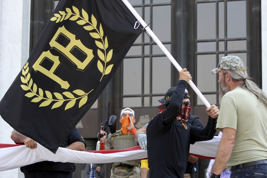 FILE - In this Sept. 7, 2020 photo, a protester carries a Proud Boys banner, symbol of a right-wing group, while other members start to unfurl a large U.S. flag in front of the Oregon State Capitol in ...