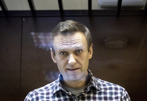 In this photo taken on Saturday, Feb. 20, 2021, Russian opposition leader Alexei Navalny looks at photographers standing behind a glass of the cage in the Babuskinsky District Court in Moscow, Russia. ...