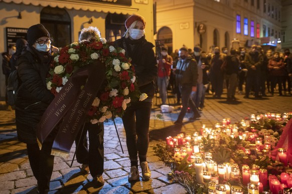 epa08798745 People carry a wreath during a candlelight vigil for the victims at the crime scene of multiple shootings in the first district of Vienna, Austria, 04 November 2020. According to recent re ...