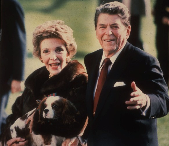 FILE - This December 1986, file photo shows first lady Nancy Reagan holding the Reagans&#039; pet Rex, a King Charles spaniel, as she and President Reagan walk on the White House South lawn. The arriv ...
