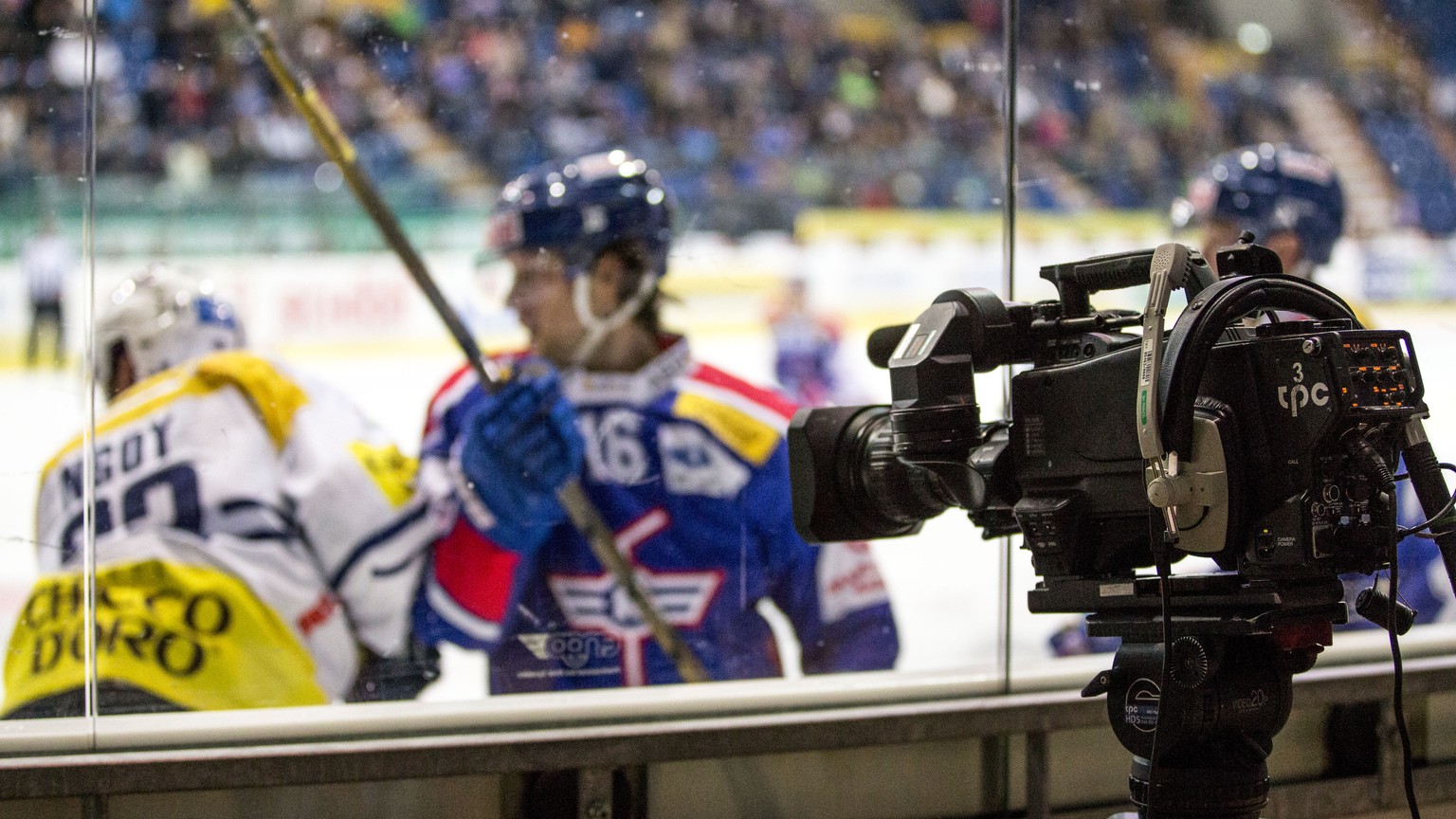 Eine TV Kamera, der Produktionsfirma tpc, steht auf einem Stativ hinter einer Glasscheibe im dritten Eishockey Spiel der Platzierungsrunde der National League A zwischen dem EHC Kloten und dem HC Ambr ...