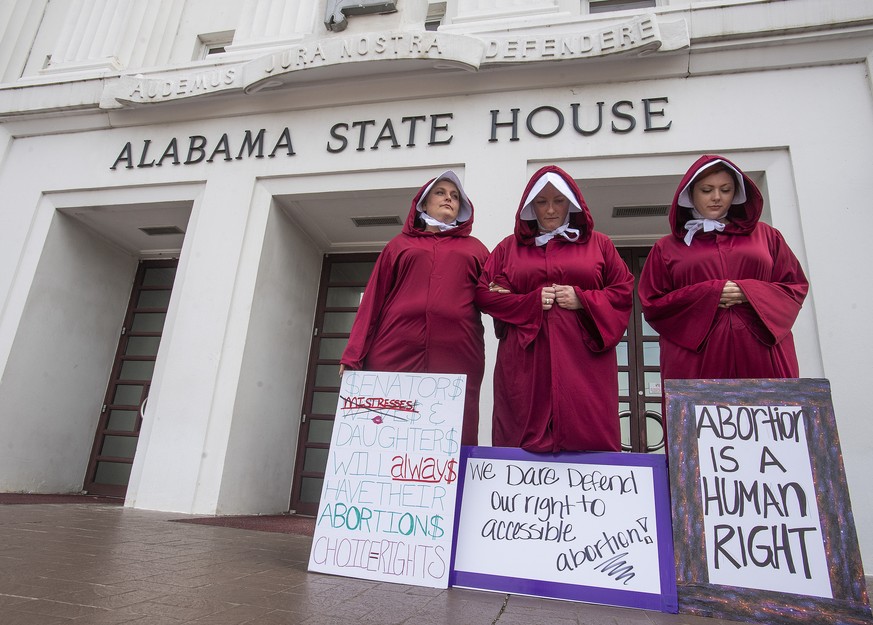 Bianca Cameron-Schwiesow, from left,Kari Crowe and Margeaux Hardline, dressed as handmaids, take part in a protest against HB314, the abortion ban bill, at the Alabama State House in Montgomery, Ala., ...