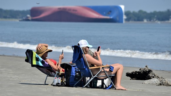 Rachel, left, and Sarah Mitchell look at their phones as they sun bathe on Jekyll Island&#039;s Driftwood Beach as the Golden Ray cargo ship is capsized in the background, off the Georgia coast, Sunda ...