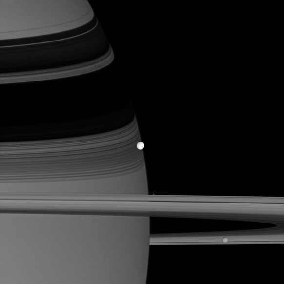 Die Saturnmonde Enceladus (hell in der Mitte), Pandora (winzig am oberen Rand der Ringe) und Mimas (unten rechts) auf einem Foto der Cassini-Sonde.&nbsp;