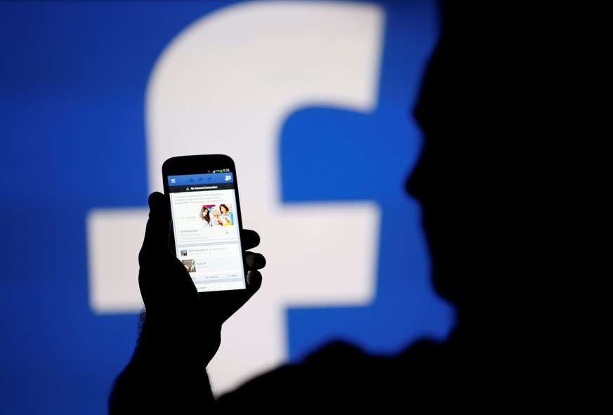 A man is silhouetted against a video screen with a Facebook logo as he poses with a Samsung S4 smartphone in this photo illustration taken in the central Bosnian town of Zenica, August 14, 2013. REUTE ...