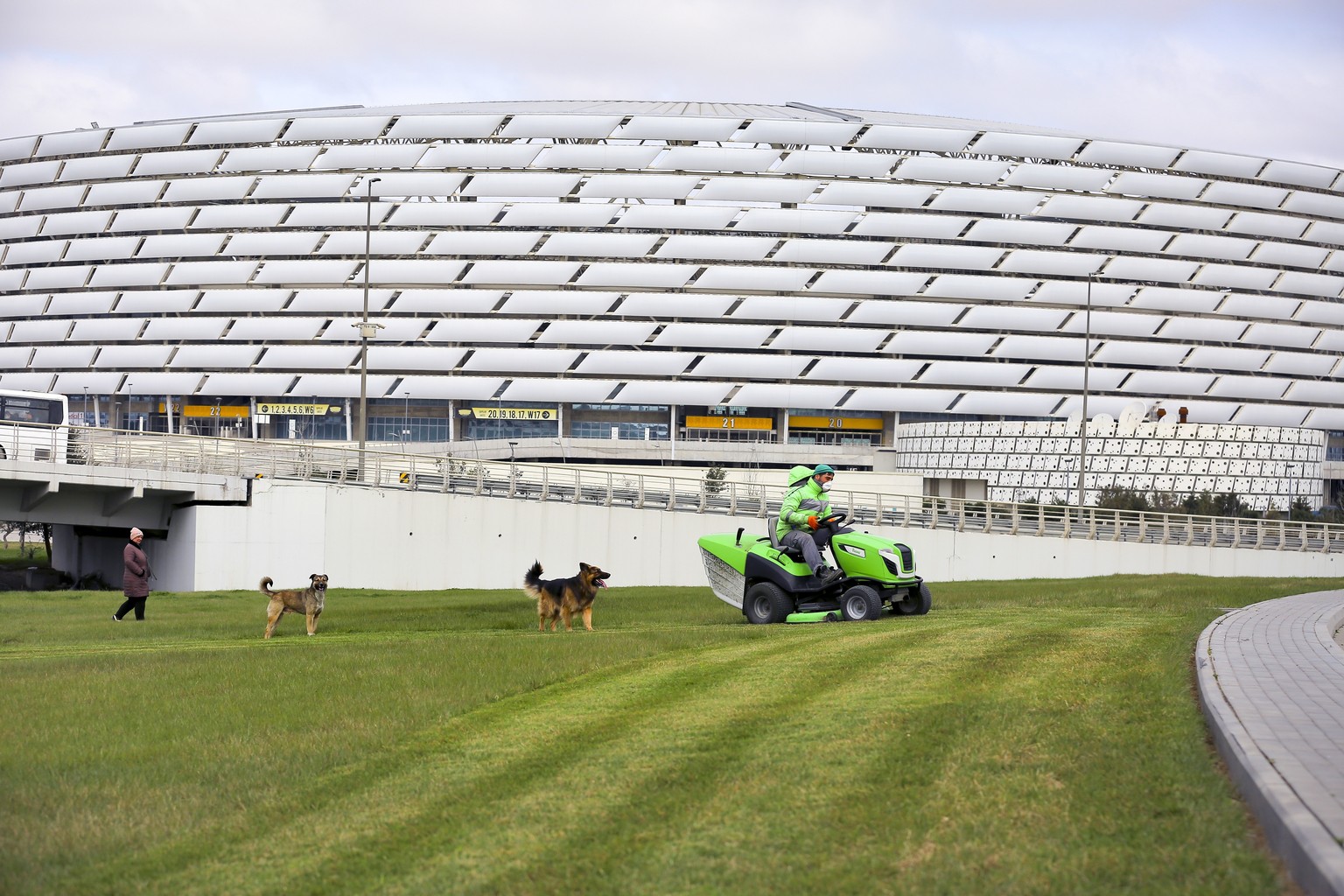 A worker rides a tractor as he mows a lawn in front of the Olympic stadium, where UEFA planned to host four UEFA Euro 2020 matches, including a quarterfinal, in Baku, Azerbaijan, Wednesday, March 18,  ...