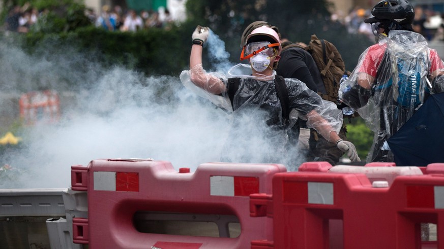 epa07643085 A protester prepares to throw back tear gas at police during a rally against an extradition bill outside the Legislative Council in Hong Kong, China, 12 June 2019. The bill has faced immen ...