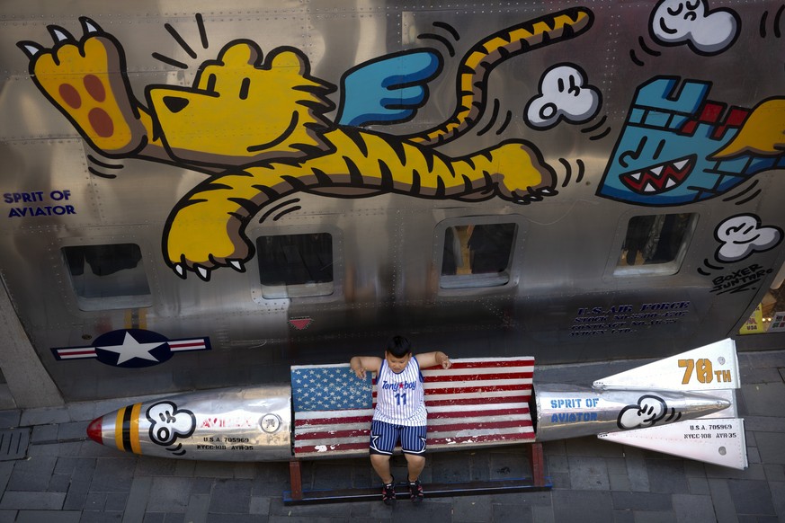 A boy sits on a bench shaped like a missile painted with the U.S. flag outside of a clothing store at a shopping mall in Beijing, Saturday, June 29, 2019. President Donald Trump and Chinese President  ...