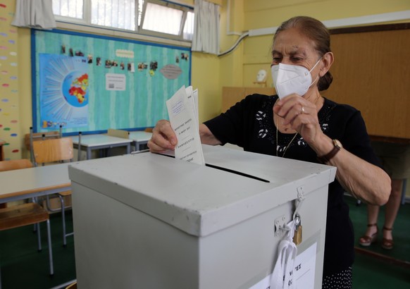 epa09236545 A Greek Cypriot woman wearing a protective face mask casts her vote in the parliamentary elections at a polling station in Nicosia, Cyprus, 30 May 2021. Cypriots go to the polls organized  ...