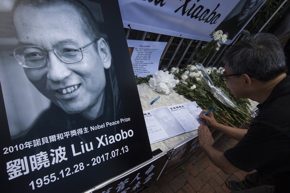 epa06086208 A member of the public signs a book of condolences and lays chrysanthemum flowers as he pays respects to the late Chinese dissident and Nobel peace laureate Liu Xiaobo at a makeshift shrin ...