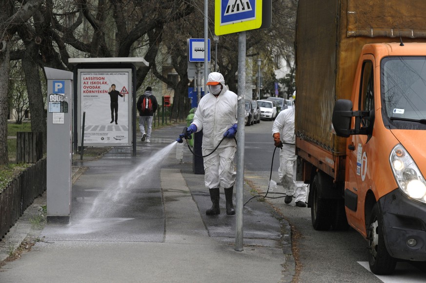 epa08331356 A municipal worker wearing protective clothing sprays disinfectant on the streets in front of a building to prevent the spread of the coronavirus in Budapest, Hungary, 30 March 2020. EPA/Z ...