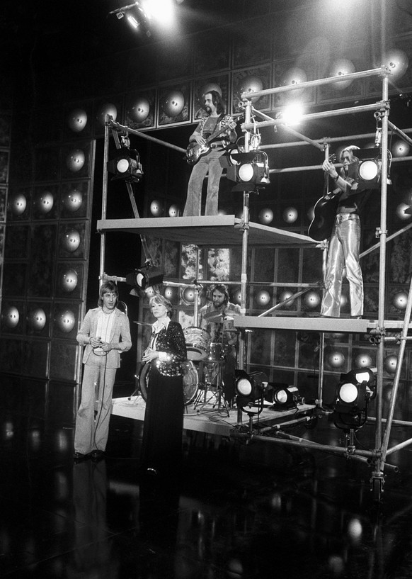 Toni Vescoli, rechts mit Gitarre und weitere Musiker treten am 6. Dezember 1975 einer Unterhaltungssendung des Schweizer Fernsehens auf. Moderiert wird die Sendung von Heidi Abel, Mitte. (KEYSTONE/Str ...