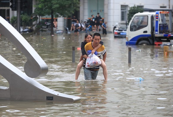 epa09356173 A man carries a woman in the flooded road after record downpours receded in Zhengzhou city in central China&#039;s Henan province, 21 July 2021. Heavy floods in Central China killed 12 in  ...