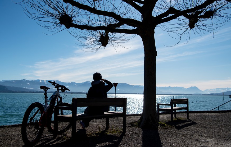 dpatopbilder - 06.02.2020, Bayern, Lindau: Eine Frau sitzt neben ihrem Fahrrad auf einer Bank am Ufer des Bodensees, und genießt das schöne Wetter. Foto: Sven Hoppe/dpa +++ dpa-Bildfunk +++