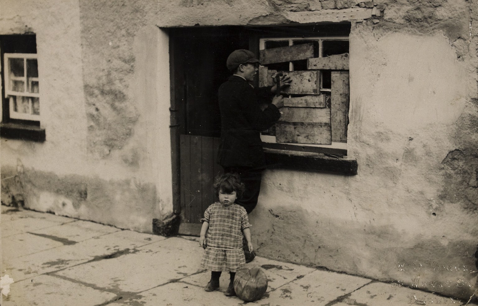 House in Templemore in aftermath of raid by Tans - boy boarding up window and child with a small ball 
This poignant shot shows a young man repairing a house that had apparently been damaged in a raid ...