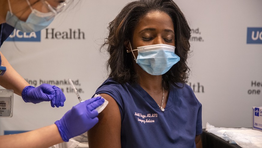 epa08888466 UCLA ER Dr. Medell Briggs-Malonson, right, closes her eyes as she gets prepped for inoculation of the Covid-19 vaccine from nurse Eunice Lee, left, at Ronald Reagan UCLA Medical Center, in ...