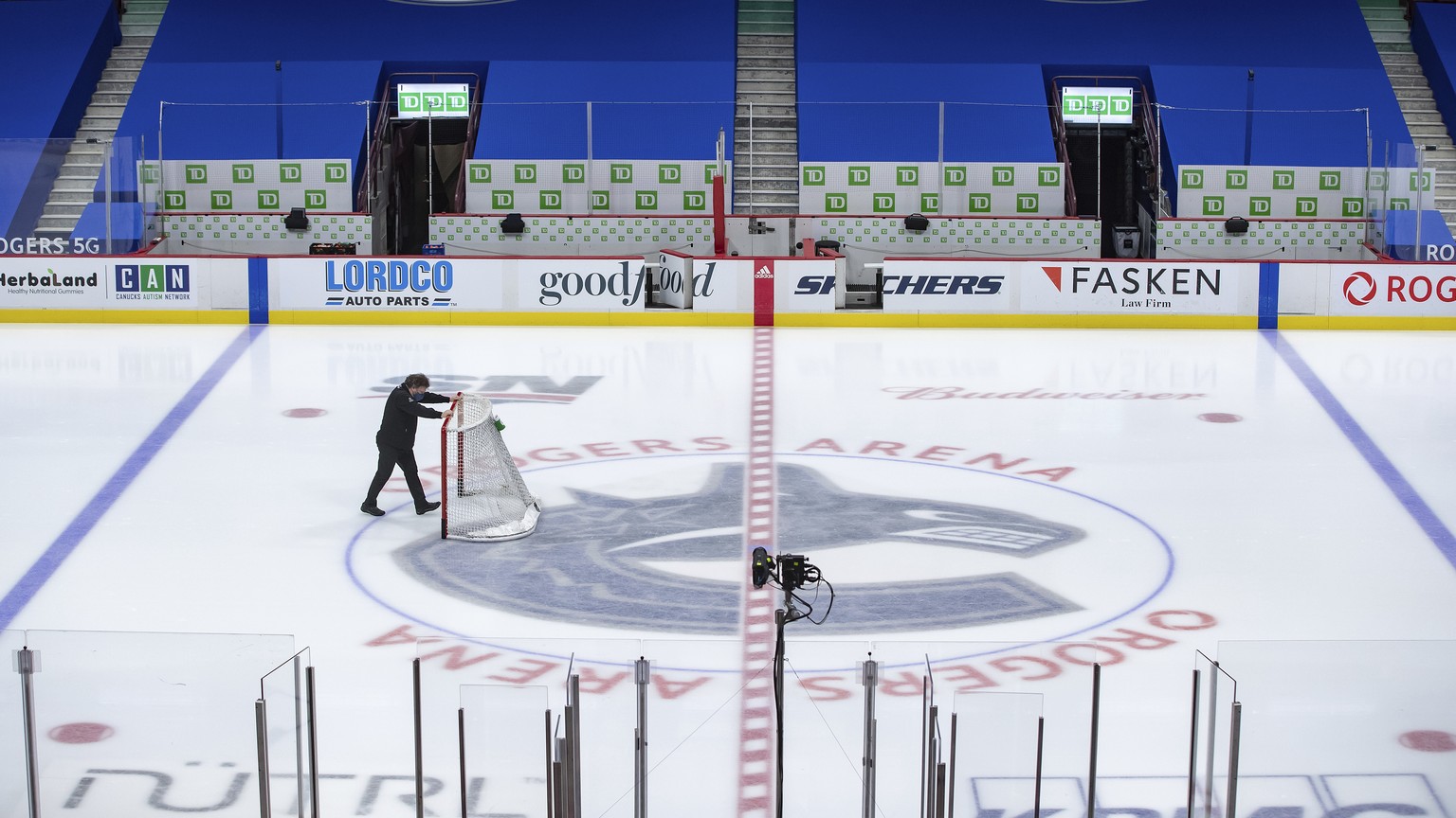 An arena worker removes the net from the ice after the Vancouver Canucks and Calgary Flames NHL hockey game was postponed due to a positive COVID-19 test result, in Vancouver, British Columbia, Wednes ...