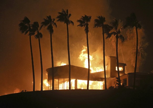 FILE - In this Nov. 9, 2018 file photo, palm trees frame a home being destroyed by the Woolsey wildfire above Pacific Coast Highway in Malibu, Calif. The 2018 wildfire that killed three people and des ...
