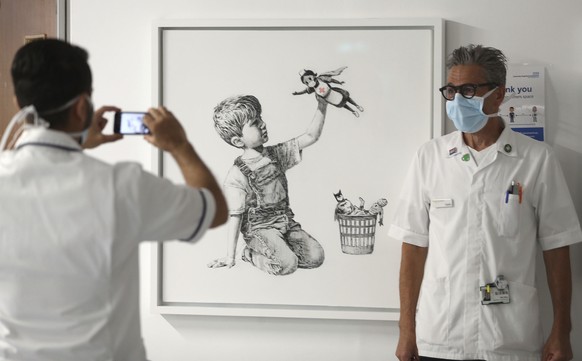 A member of staff has their photograph taken in front of the new artwork painted by Banksy during lockdown, entitled &#039;Game Changer&#039;, which has gone on display to staff and patients on Level  ...