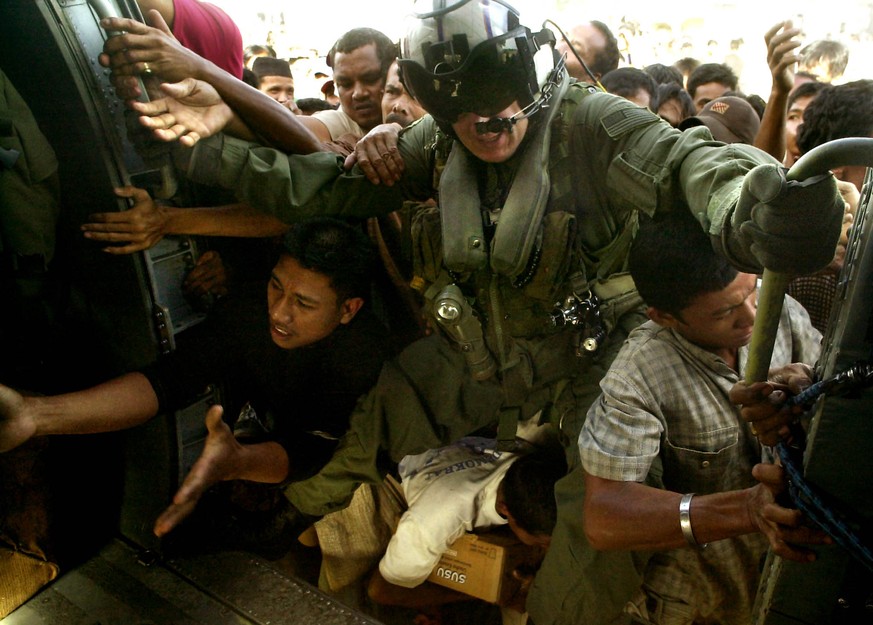 FILE - In this Jan. 8, 2005 file photo, US Navy AW2 Maxwell Bjeule (no state given) tries to restrain a surging crowd of survivors as they struggle to get food and other supplies being unloaded from a ...