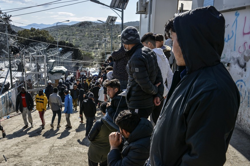 Migrants gather as riot police guard a gate in Moria refugee camp on the northeastern Aegean island of Lesbos, Greece, Monday, March 16, 2020. The Fire Service said a migrant, who was not further iden ...