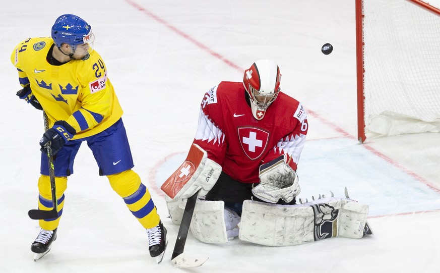 epa09227368 Switzerland&#039;s goaltender Leonardo Genoni (R) turns away the puck past Sweden&#039;s forward Oscar Lindberg during the IIHF 2021 ICe Hockey World ChampionshipGroup A match between Swit ...