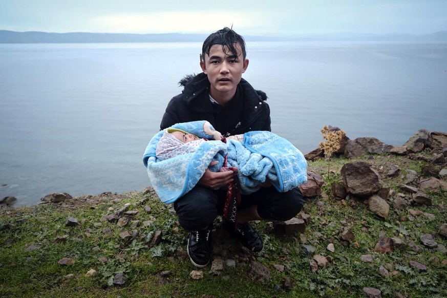 A migrant holding a baby pauses on the side of the road while walking to the village of Skala Sikaminias, on the Greek island of Lesbos, after crossing on a dinghy the Aegean sea from Turkey on Thursd ...