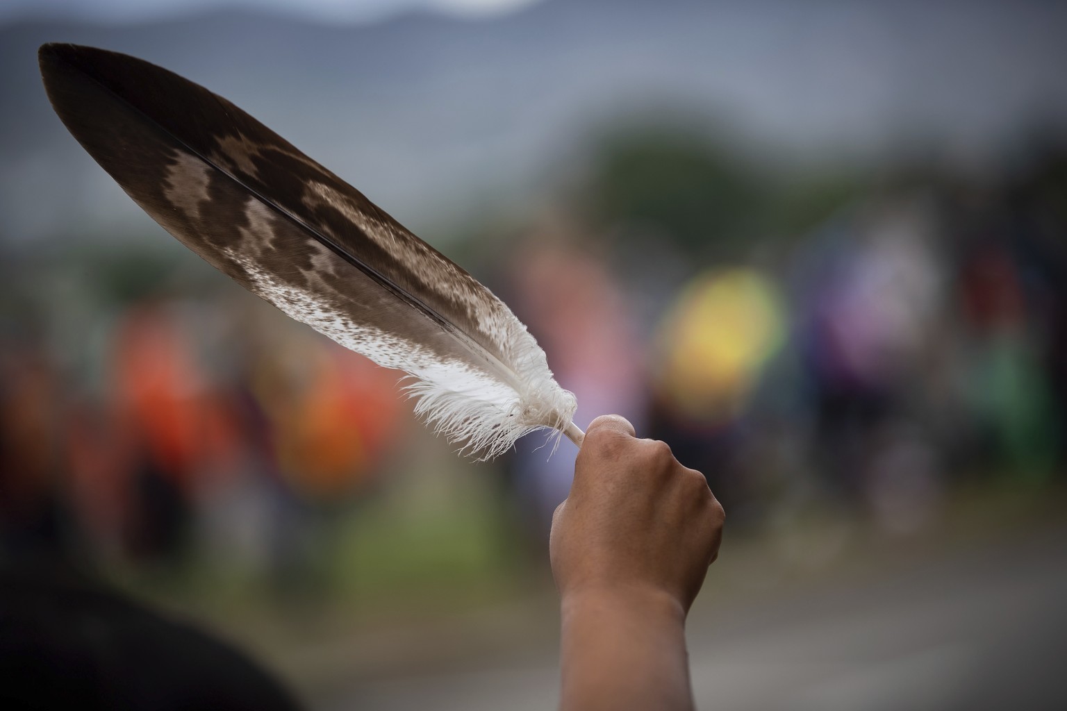 A woman holds an eagle feather while watching a convoy of truckers and other vehicles travel past in support of the Tk&#039;emlups te Secwepemc people, after the remains of 215 children were discovere ...
