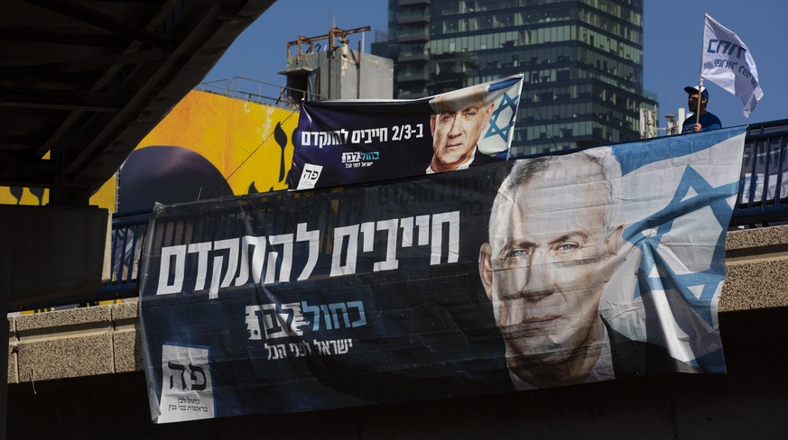 Blue and White party activist waves a flag behind an election campaign billboard that shows the party&#039;s leader Benny Gantz, in Tel Aviv, Israel, Sunday, March. 1, 2020. Israel heads into its thir ...