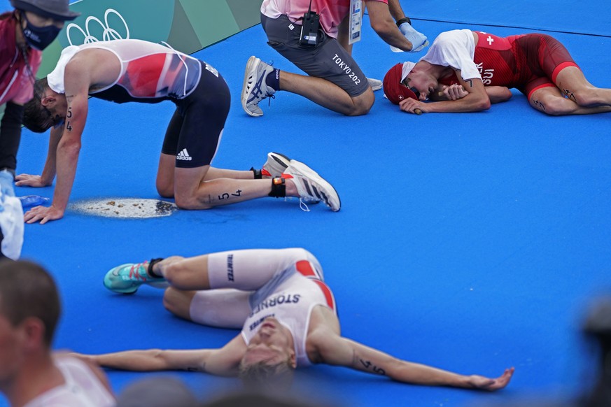 Casper Stornes of Norway (45), Jonathan Brownlee of Great Britain (54) and Max Studer of Switzerland (47) all collapse after crossing the finish line at the men&#039;s individual triathlon during the  ...