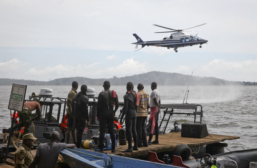 Ugandan divers look up as a helicopter searches for victims of a boat which capsized in Lake Victoria near the capital, Kampala, Uganda, Sunday, Nov. 25, 2018. Ugandan diving teams are retrieving bodi ...