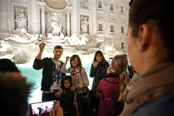 epa05009485 People flip coins as they have their souvenir photo taken in front of the landmark Trevi Fountain after its restoration in Rome, Italy, 03 November 2015 evening. The Trevi Fountain, one of ...