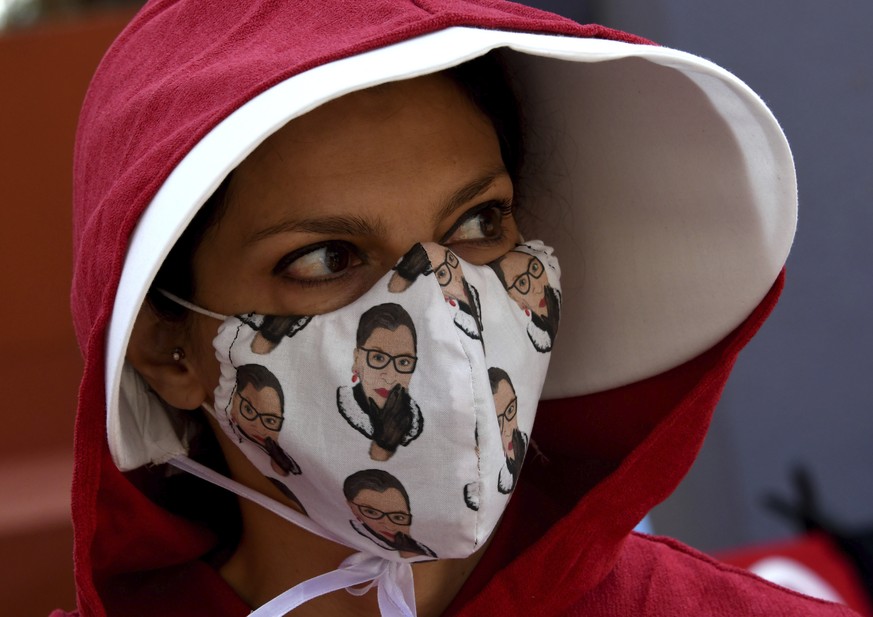 A woman wearing a Handmaid&#039;s Tale outfit and Ruth Bader Ginsburg mask protest along with hundreds on many issues including the Trump Administration&#039;s efforts to replace the late Supreme Cour ...