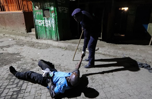 epa08335550 A Kenyan police officer (R), helps a drunk man to standup after they found him in the middle of the road as they patrolled at night to enforce that people are in their homes during the cur ...