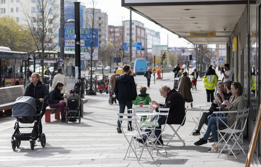 People eat ice cream at an outdoor cafe as others pass by in central Stockholm, Sweden, Monday April 20, 2020 during the coronavirus (COVID-19) outbreak. (Ali Lorestani/TT via AP)